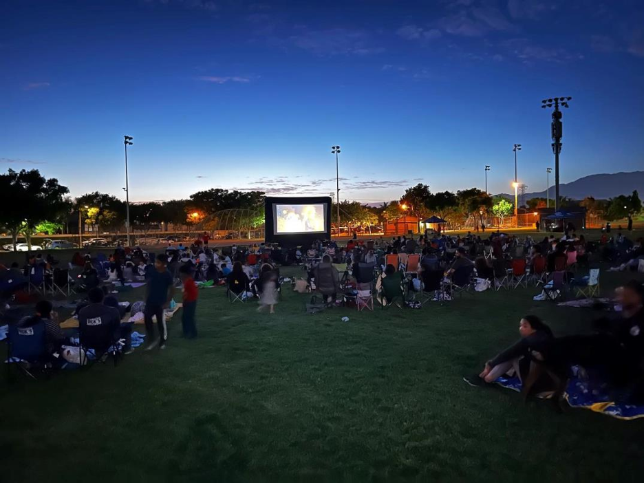 People gather around movie screen in a park